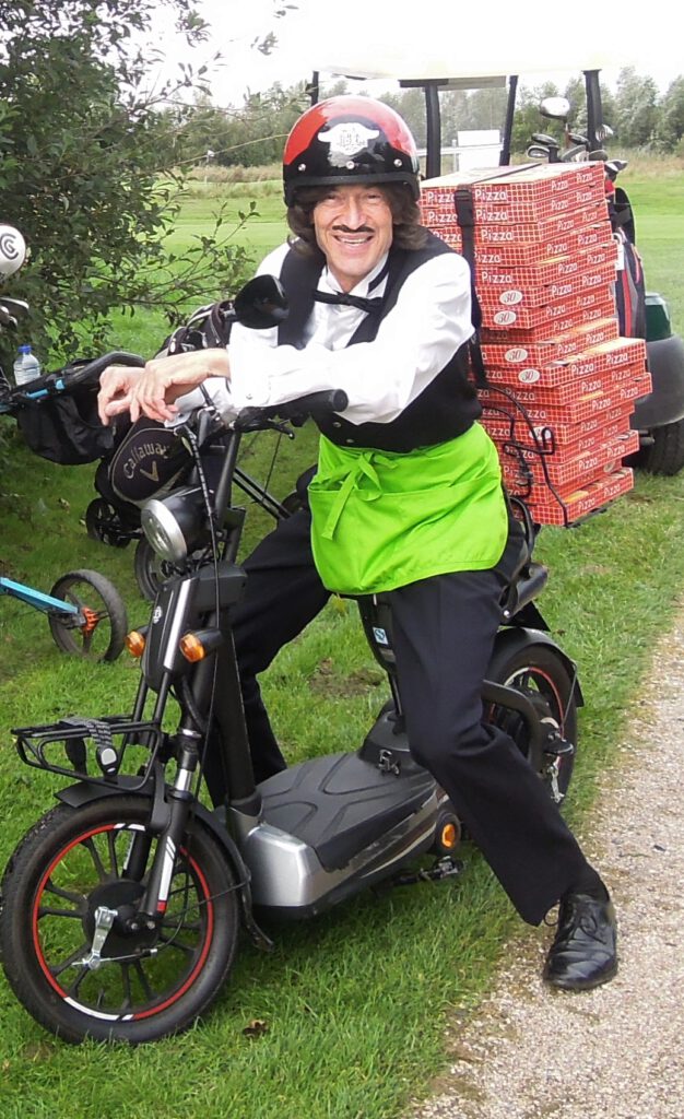 Typetje pizzakoerier stat met zijn scooter op gras