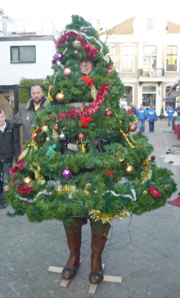 Typetje wandelende kerstboom staat buiten op een markt.